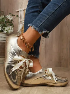 Detailed close-up of shiny metallic gold retro sneakers featuring elegant white ribbon laces