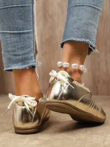 Close-up of gold metallic sneakers with elegant white ribbon bow laces and flat sole