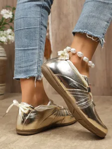 Close-up of shiny metallic gold retro sneakers with elegant white ribbon laces
