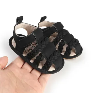 Close-up detail of a black braided baby sandal held in hand to showcase material and scale