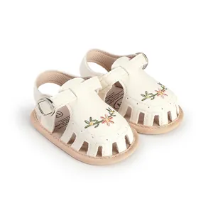 Dettaglio di sandali bianchi per neonata con delicato ricamo floreale e design traforato.