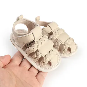 Close-up of beige braided infant sandals with hook-and-loop strap held in a hand