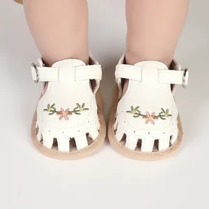 Primo piano di sandali in pelle bianca per neonata con ricamo floreale e cinturino