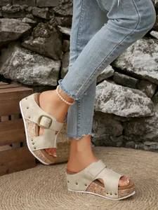 Detailweergave van beige sleehaksandalen met kurkzool en gesp, gedragen door model.