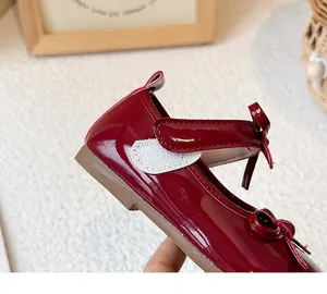 Close-up of red patent leather girl's shoe with white Velcro strap and bow detail.