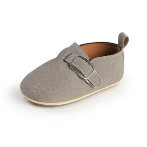 Close-up of retro grey suede baby shoes with silver buckle detail on white background.
