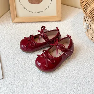Shiny burgundy girls' Mary Janes with adorable bow detail on textured white rug