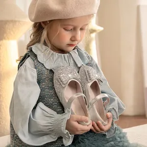 Elegant sparkling silver girl's Mary Jane shoes with rhinestone bow held by a child.