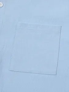 Macro detail shot showing the pocket stitching and linen fabric texture of a light blue shirt.
