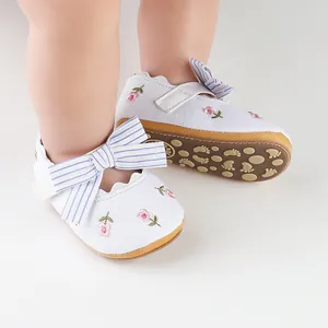 Dettaglio scarpe per neonata con ricami floreali, fiocchi a righe e suole morbide