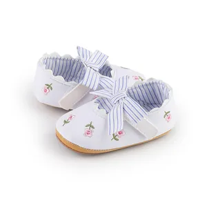 Primo piano di scarpe bianche per neonati con ricamo a fiori e dettaglio di fiocco a righe blu
