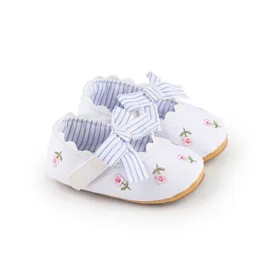 Dettaglio del ricamo floreale e del fiocco a righe sulle scarpe da principessa per neonati