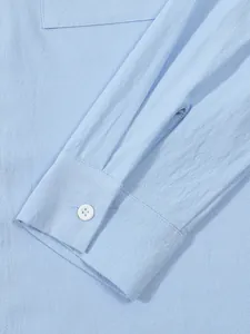 Close-up of light blue cotton-linen shirt sleeve detail showing button and fabric texture.