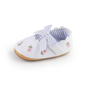 Dettaglio di una scarpa primi passi per neonata bianca con ricami floreali e fiocco.