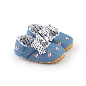 Dettaglio scarpe neonata in denim blu con ricami floreali rosa e fiocco a righe bianche e nere