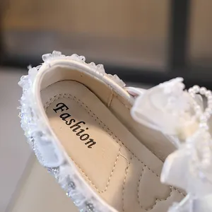 Primer plano zapatos de princesa blancos para niña con lazo de perlas y diamantes