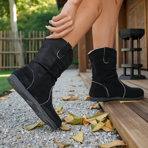 Close-up of black suede slouchy ankle boots with white stitching on outdoor deck.