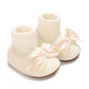 Macro view of cream baby girl lace sock shoes featuring elegant ribbon bows and soft knit cuffs