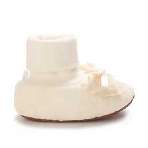 Detailed view of cream baby sock shoe with lace patterns and silk bow decoration