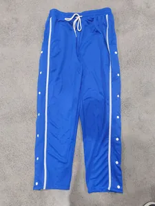 Detalle de pantalones deportivos azules con botones de presión laterales blancos.