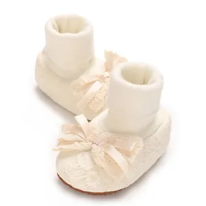 Detail view of cream baby sock shoes with lace patterns and ribbon bow accents