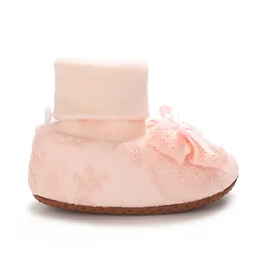 Close-up detail of pink baby girl sock shoe with lace embroidery and a delicate bow.
