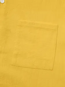 Macro detail of a yellow men's cotton linen shirt showing pocket and fabric texture