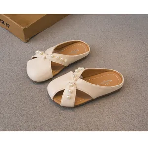 Primer plano de elegantes pantuflas crema para niñas con perlas y un lazo anudado.