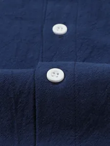 Close-up detail of the white buttons and textured fabric of a navy blue cotton linen shirt