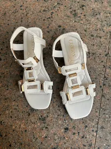 Detailed view of white Roman style flat sandals with golden decorative hardware.