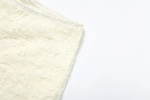 Close-up detail of cream textured lace fabric showing intricate hollow-out patterns