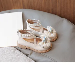 Macro detail of girls' cream princess shoes featuring rhinestone bow and pearl straps.