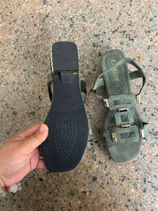 Close-up of green Roman flat sandals showing non-slip sole and gold buckle straps.