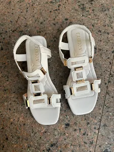 Close-up top view of white Roman style sandals with gold metallic accents on stone