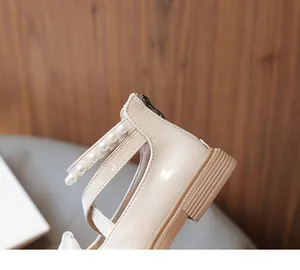 Close-up of girls' beige patent leather princess shoes with pearl strap and back zipper.