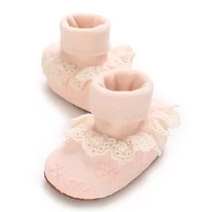 Detalle de patucos rosa para bebé niña con volante de encaje blanco y bordado floral.