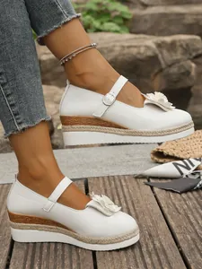 Primer plano elegante de zapatos con cuña blancos, detalle de flor y suela de esparto.