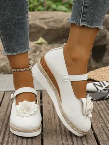 Primer plano de Mary Janes blancas de plataforma con flores y suela de cuerda.