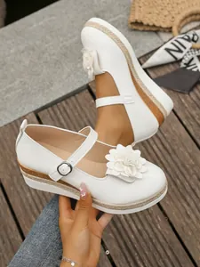 Detalle de zapatos Mary Jane blancos con cuña, flor grande y suela de plataforma de yute