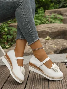 Primer plano de zapatos Mary Jane blancos con cuña con flores y plataforma de cuerda de cáñamo