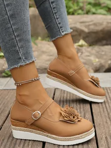 Vista lateral de zapatos Mary Jane marrones con cuña, flores y plataforma trenzada