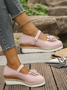 Vista detallada de zapatos de cuña rosa con adornos florales y correas.