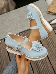 Vista detallada de zapatos de cuña azul claro con decoración floral y ribete de yute trenzado