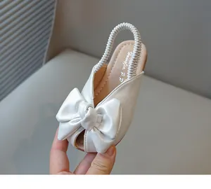Close-up of white girls' sandals featuring a large leather bow and peep-toe design