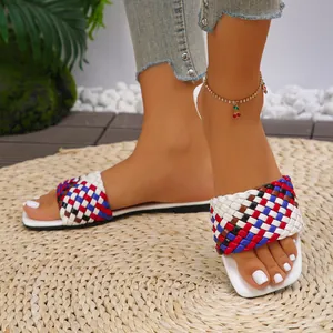 Macro detail view of stylish colorful woven square-toe flat slippers worn on a straw mat