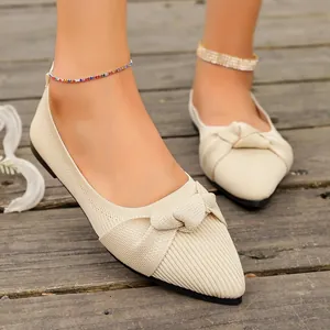 Eleganti ballerine beige in maglia con punta e fiocco decorativo su sfondo di legno