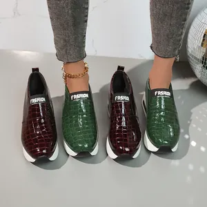Dettaglio di sneaker slip-on da donna con trama coccodrillo e suole bianche spesse.