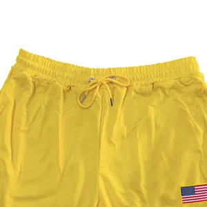 Detailopname van een gele joggingbroek met trekkoord en een Amerikaanse vlag patch.