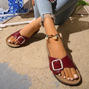 Gros plan de sandales bordeaux à motif croco avec boucle argentée vintage sur le sable