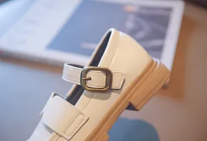 Close-up of white Mary Jane shoes with bronze buckle and neat stitching details